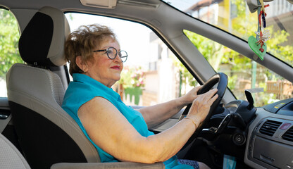 Obraz premium Beautiful lady in a blue shirt in her 70s is driving a car