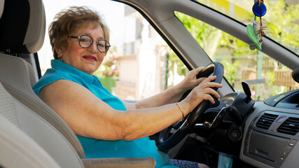 Obraz premium Beautiful lady in a blue shirt in her 70s is driving a car