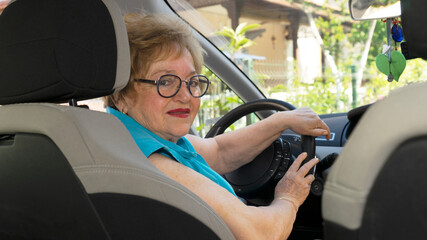 Beautiful lady in a blue shirt in her 70s is driving a car
