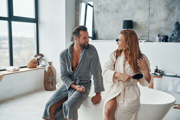 Couple in bathrobes smiling and cleaning teeth while doing morning routine
