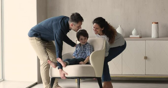 Parents carry new comfy chair where their little son is sit. Happy homeowner family make permutation. Relocating at own first flat. Remodeling, renovation, fashionable modern furnish store ad concept