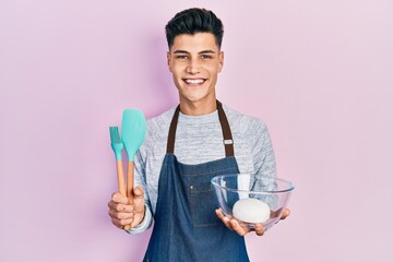 Young hispanic man holding bread dough and cooking tools smiling with a happy and cool smile on face. showing teeth.