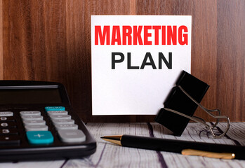 MARKETING PLAN is written on a white card on a wooden background next to a calculator and pen.