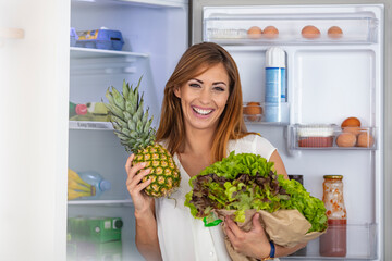Healthy Eating Concept. Diet. Beautiful Young Woman near the Fridge with healthy food. Fruits and Vegetables in the Refrigerator. Vegan food. Young woman with purchase box full of vegetables  - Powered by Adobe