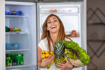 Young woman with fruits and vegetables beside fridge in kitchen. purchase box full of vegetables...