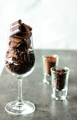 Different kinds of chocolates in wine glass and shot glasses with copy space on light background; creative food design; dark and milk chocolate pieces