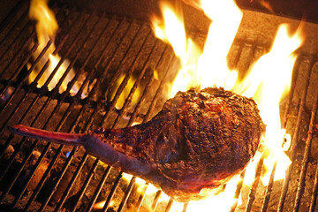 Tomahawk Rib eye on a grill, surrounded by flames. Searing the steak, at high temperature before cooking at a reduced heat. Extra thick cut of ribeye steak on a grill top.