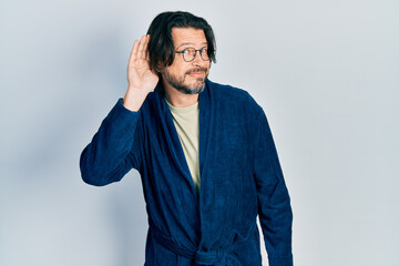 Fototapeta premium Middle age caucasian man wearing bathrobe and glasses smiling with hand over ear listening an hearing to rumor or gossip. deafness concept.