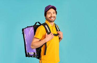Portrait of a young courier, delivery man in uniform with a thermo backpack isolated on a blue background. Fast home delivery. Online order.