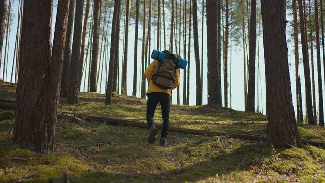African black man climbs uphill in woods in yellow jacket with backpack in slow motion
