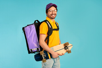 Young courier delivery man in uniform with thermo backpack and skate isolated on blue background. Fast express home delivery. Online order.