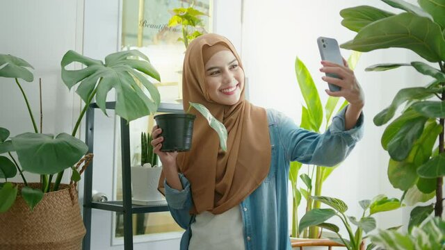Happy young muslim woman taking selfie with her plants and making video call at home