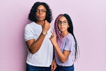 Beautiful african american mother and daughter wearing casual clothes and glasses in hurry pointing to watch time, impatience, looking at the camera with relaxed expression