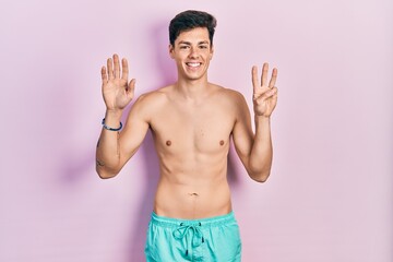 Fototapeta premium Young hispanic man wearing swimwear shirtless showing and pointing up with fingers number eight while smiling confident and happy.