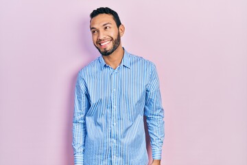 Hispanic man with beard wearing casual blue shirt looking away to side with smile on face, natural expression. laughing confident.