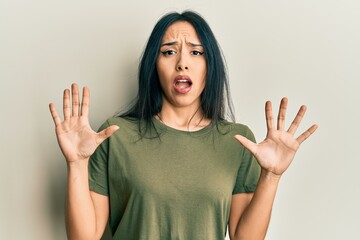 Young hispanic girl wearing casual t shirt afraid and terrified with fear expression stop gesture with hands, shouting in shock. panic concept.