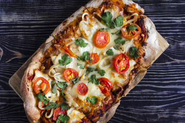 Fresh pinsa with tomatoes and herbs on a dark wood background top view. Pinsa home cooking. Pizza pastries