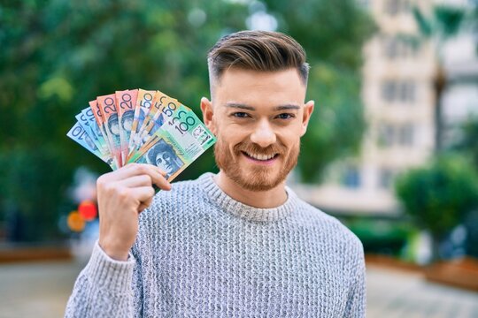 Young caucasian man smiling happy holding australian dollars at the park.