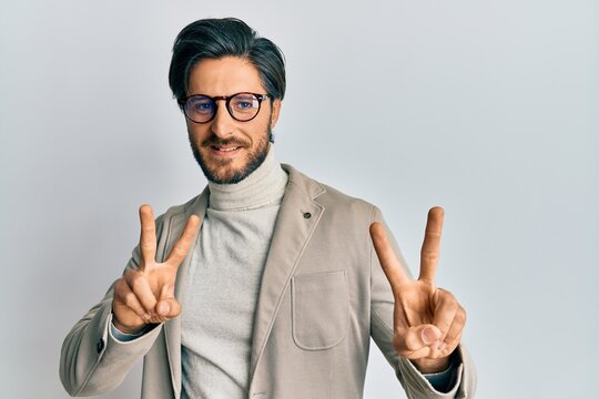 Young hispanic man wearing business jacket and glasses smiling looking to the camera showing fingers doing victory sign. number two.