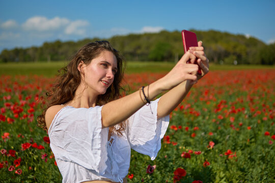 young woman taking a selfie in a field of red poppies