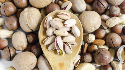 Pistachio nuts in a wooden spoon on the background of a scattering of different nuts assorted nuts	