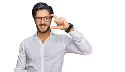 Young hispanic man wearing business shirt and glasses smiling and confident gesturing with hand doing small size sign with fingers looking and the camera. measure concept.