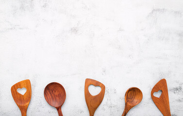 Various heart shape of wooden cooking utensils. Wooden spoons and wooden spatula on white concrete...