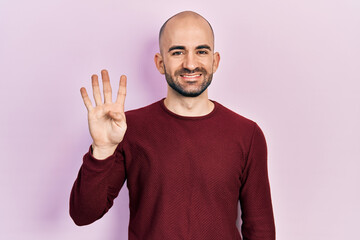 Fototapeta premium Young bald man wearing casual clothes showing and pointing up with fingers number four while smiling confident and happy.