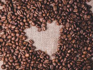 Roasted coffee beans background. Arabica beans on a jute bag. Macro texture of jute cloth with coffee beans on it. Heart shape from coffe beans.