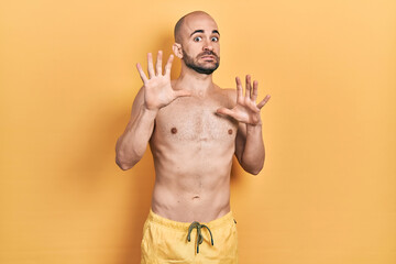 Fototapeta premium Young bald man wearing swimwear afraid and terrified with fear expression stop gesture with hands, shouting in shock. panic concept.