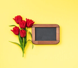 Bouquet  red tulips and chalk  note board on yellow background, top view