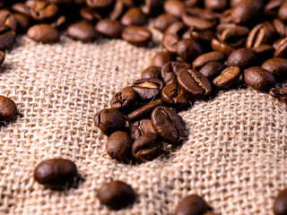 Roasted coffee beans background. Arabica beans on a jute bag. Macro texture of jute cloth with coffe beans on it.