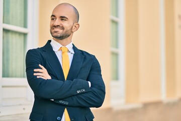 Young hispanic bald businessman with arms crossed smiling happy at the city.