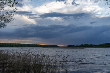 Evening landscape with a river and clouds. Dramatic sunset over the river. Dry grass in the river.