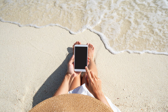 Young woman using mobile phone at beautiful tropical white sand beach with wave foam and transparent sea, Summer vacation and Travel concept with copy space