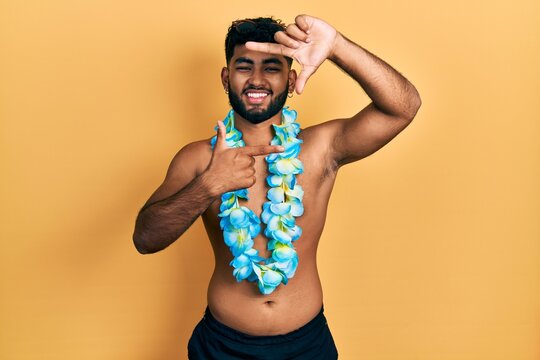 Arab man with beard wearing swimsuit and hawaiian lei smiling making frame with hands and fingers with happy face. creativity and photography concept.
