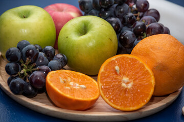 Oranges, apples, and grapes on a wooden platter are fruits with fresh vitamins, nutritionists recommend. 