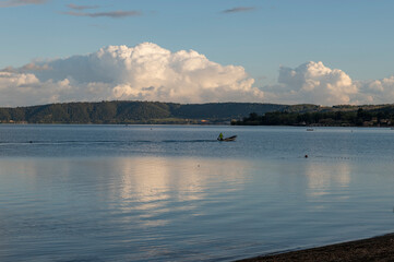 Pescatore tra le nuvole riflesse, lago di Bracciano, Lazio, Italia.