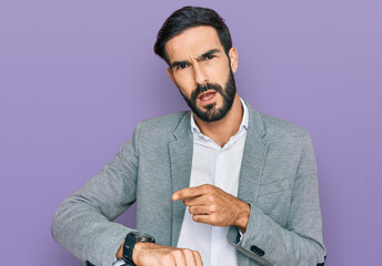 Young hispanic man wearing business clothes in hurry pointing to watch time, impatience, upset and...