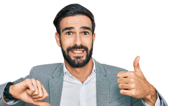 Young hispanic man wearing business clothes doing thumbs up and down, disagreement and agreement expression. crazy conflict