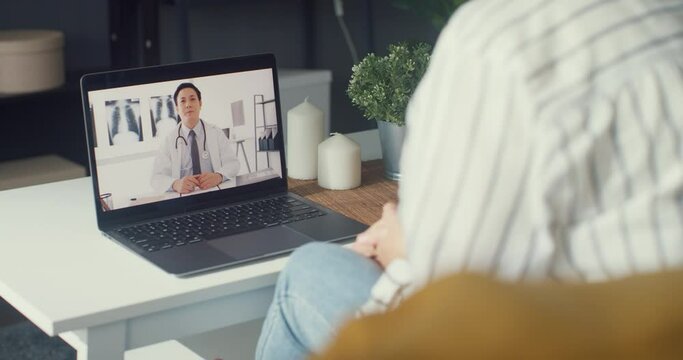 Young Asia girl using computer laptop talk about disease in video conference call with senior doctor online consultation in living room at house. Social distancing, quarantine for coronavirus concept.
