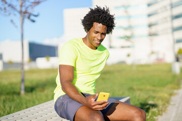 Fototapeta premium Black man consulting his smartphone with some exercise app while resting from his workout.