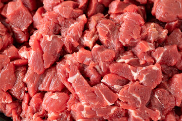 Chopped raw veal meat cubes for saute on white wooden table. Raw Meat backround. Close up meat