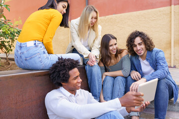 Multi-ethnic group of young people looking at a digital tablet outdoors in urban background.