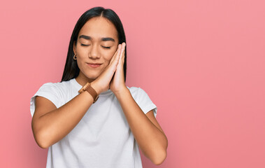 Young asian woman wearing casual white t shirt sleeping tired dreaming and posing with hands together while smiling with closed eyes.