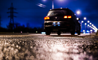 Rainy night in the big city, the big black car parked on the roadside. Close up view from the asphalt level