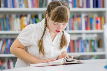 Young girl with syndrome down reads a book at library. Education for disabled children concept