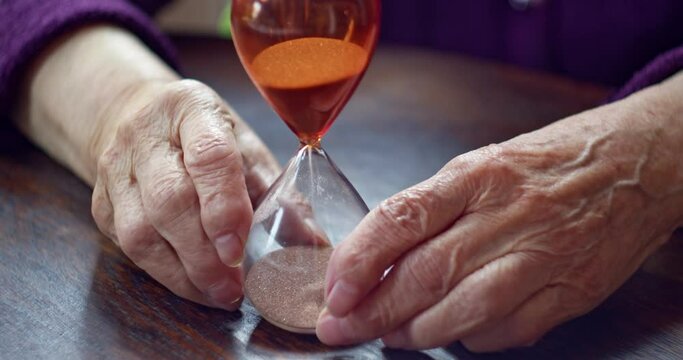 hourglass in the hands of an elderly man. the time that goes by. the danger of procrastination and transience of life. 