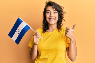 Young hispanic woman holding honduras flag smiling happy and positive, thumb up doing excellent and...