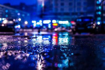 Rainy night in the big city, the street with bright shop windows. Close up view of a puddle on the asphalt level